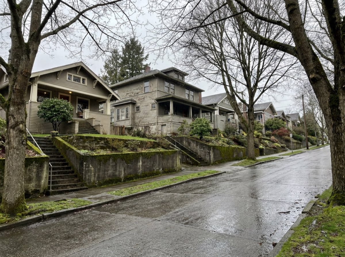 Craftsman houses stepped up a steep, wet Seattle street behind mossy concrete retaining walls and stairs